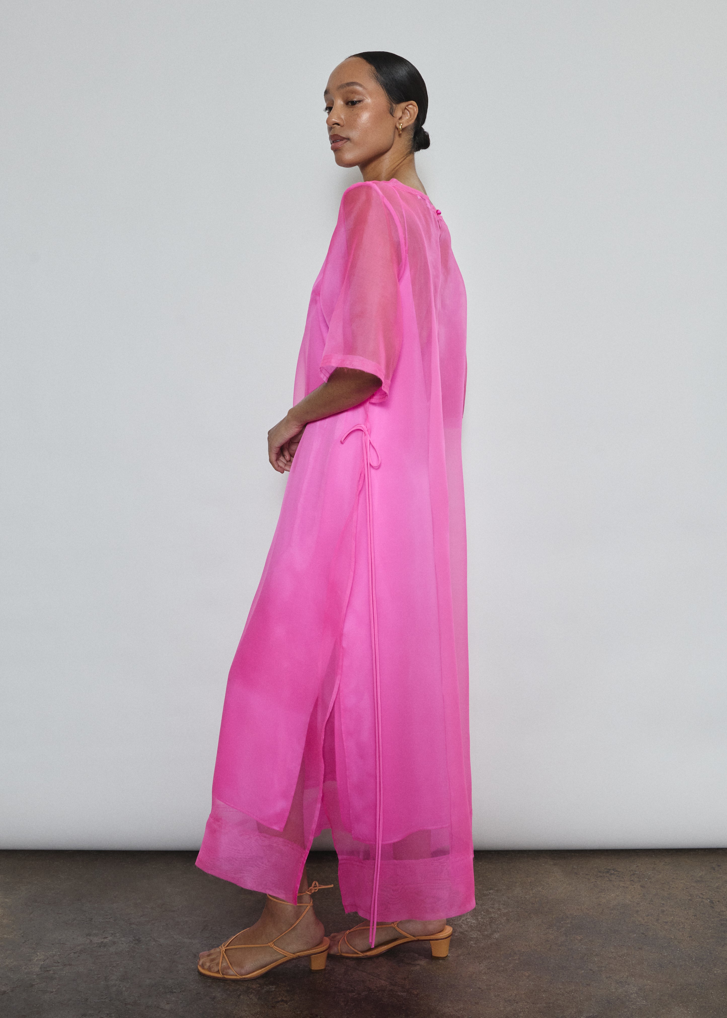 Left profile of hot pink silk organza Thea Sheath Dress. Straight-cut minimalist silhouette glows in saturated silk. Elevated luxury occasion wear, designed in San Francisco.