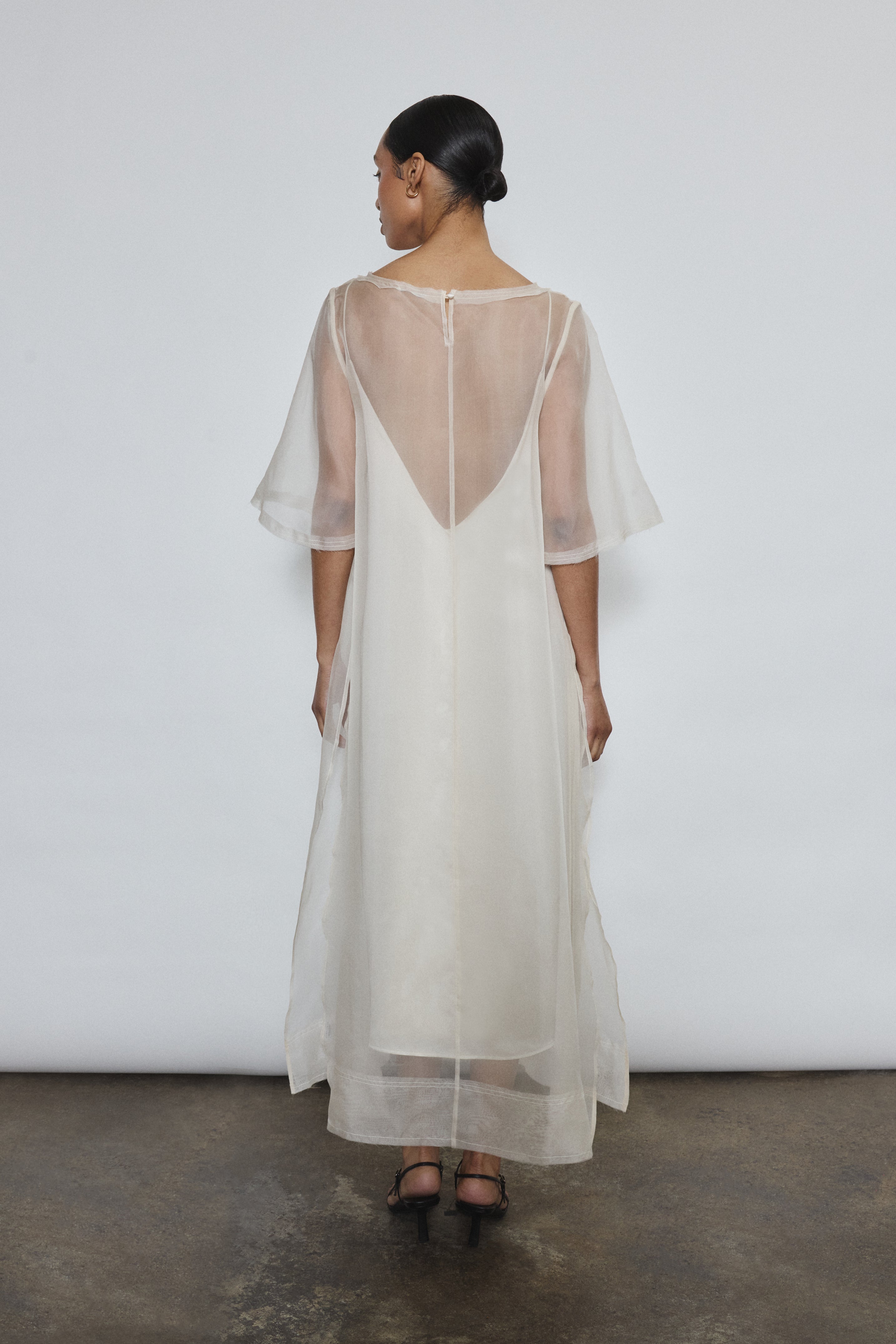 Rear view of ivory silk organza Thea Sheath Dress showing open side seams and wide hem facing. Clean architectural lines, ethically made in California.