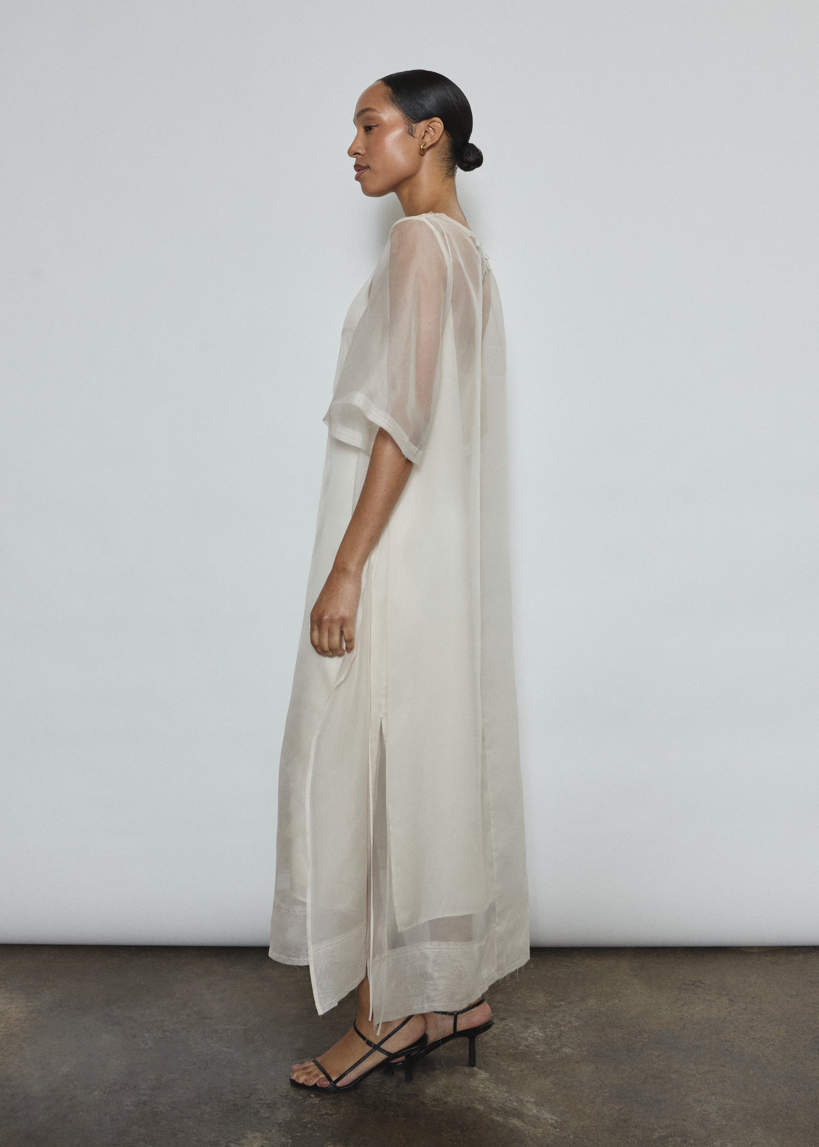 Left profile of ivory silk organza midi dress. Straight-cut minimalist silhouette with raw edge hem. Whisper-weight construction, designed in San Francisco.