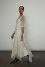 Left profile of ivory silk organza midi dress. Straight-cut minimalist silhouette with raw edge hem. Whisper-weight construction, designed in San Francisco.