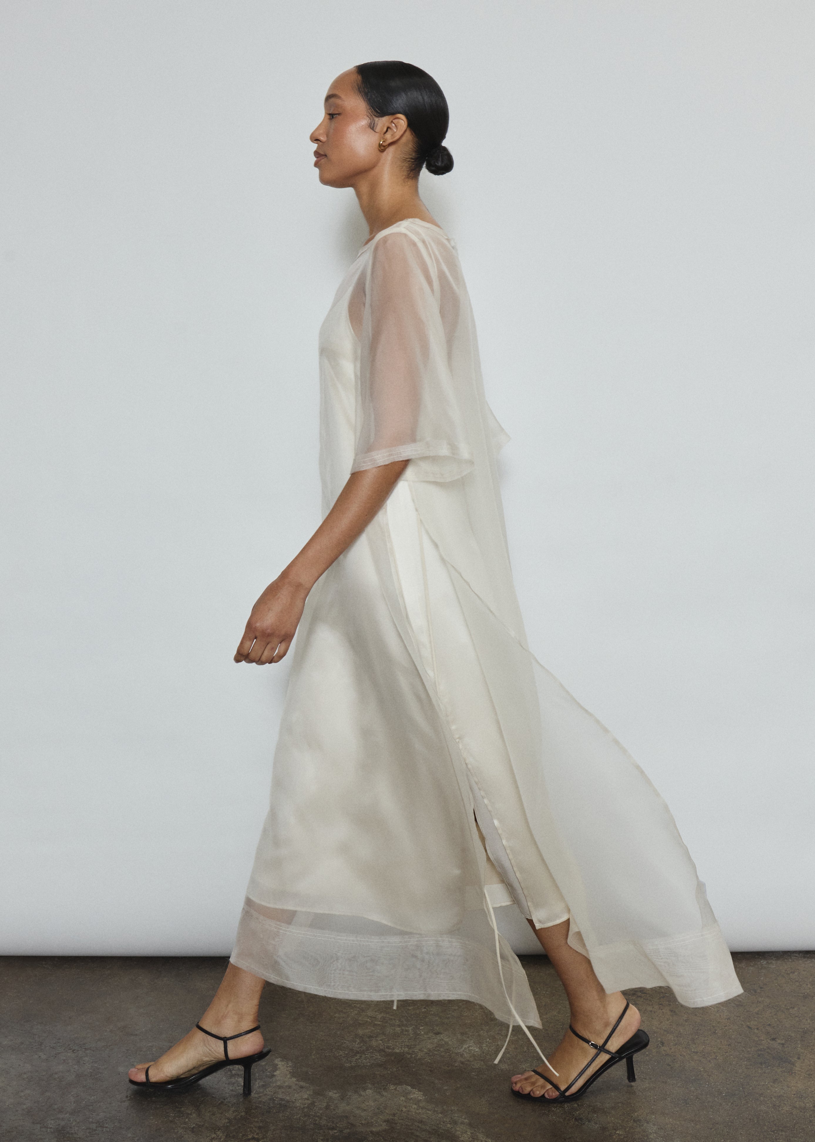 Left profile of ivory silk organza midi dress. Straight-cut minimalist silhouette with raw edge hem. Whisper-weight construction, designed in San Francisco.