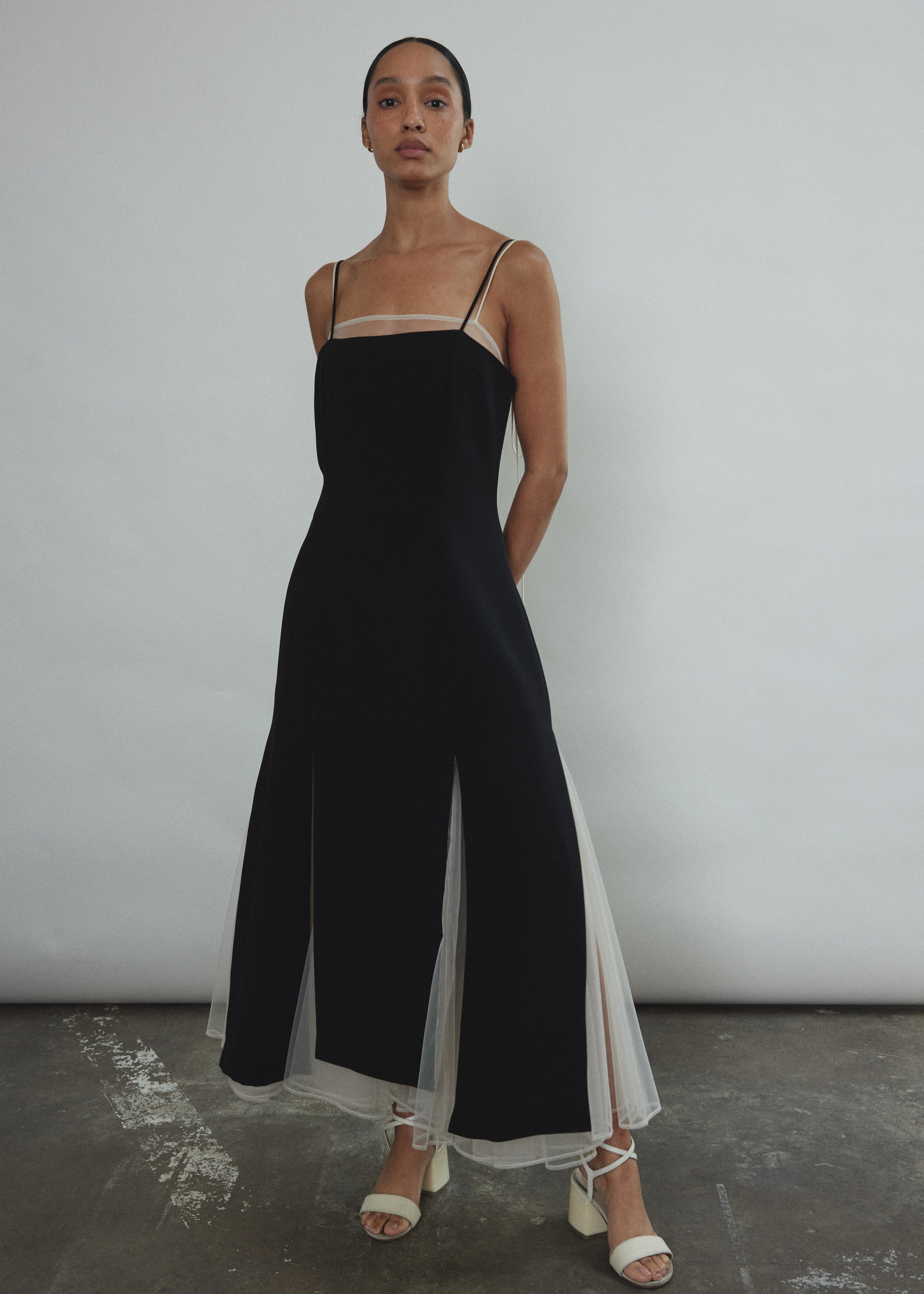 Front view of a model wearing the black crepe Kamperett Theodora Dress, a midi slip with multi-slit hemline.