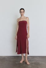 Front view of a model wearing the bordeaux silk Kamperett Theodora Dress, a sleek midi slip dress with multi-slit hemline.