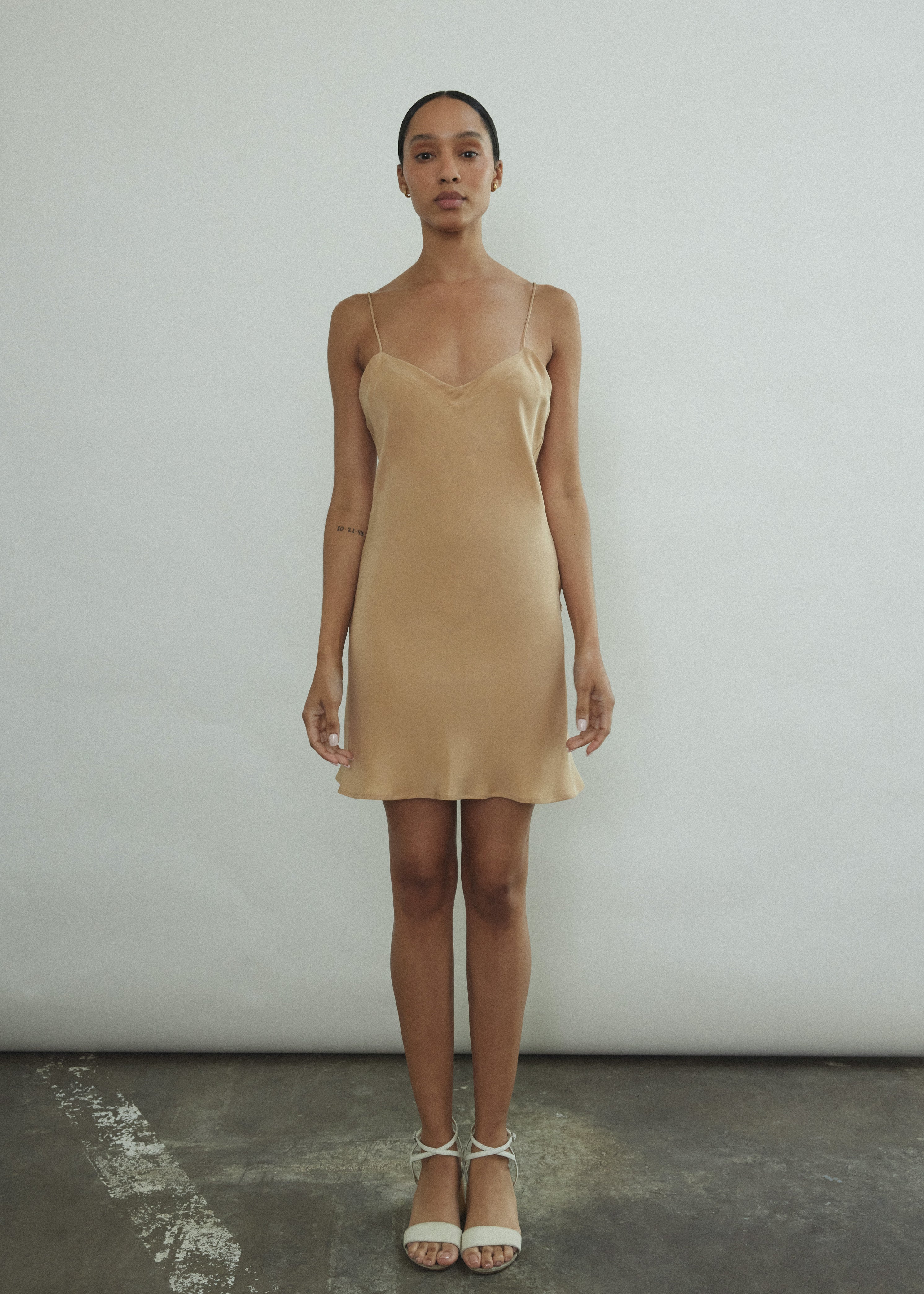 Front view of a model wearing the buff silk Kamperett V-Neck Mini Slip, a bias-cut mini with V-neckline.