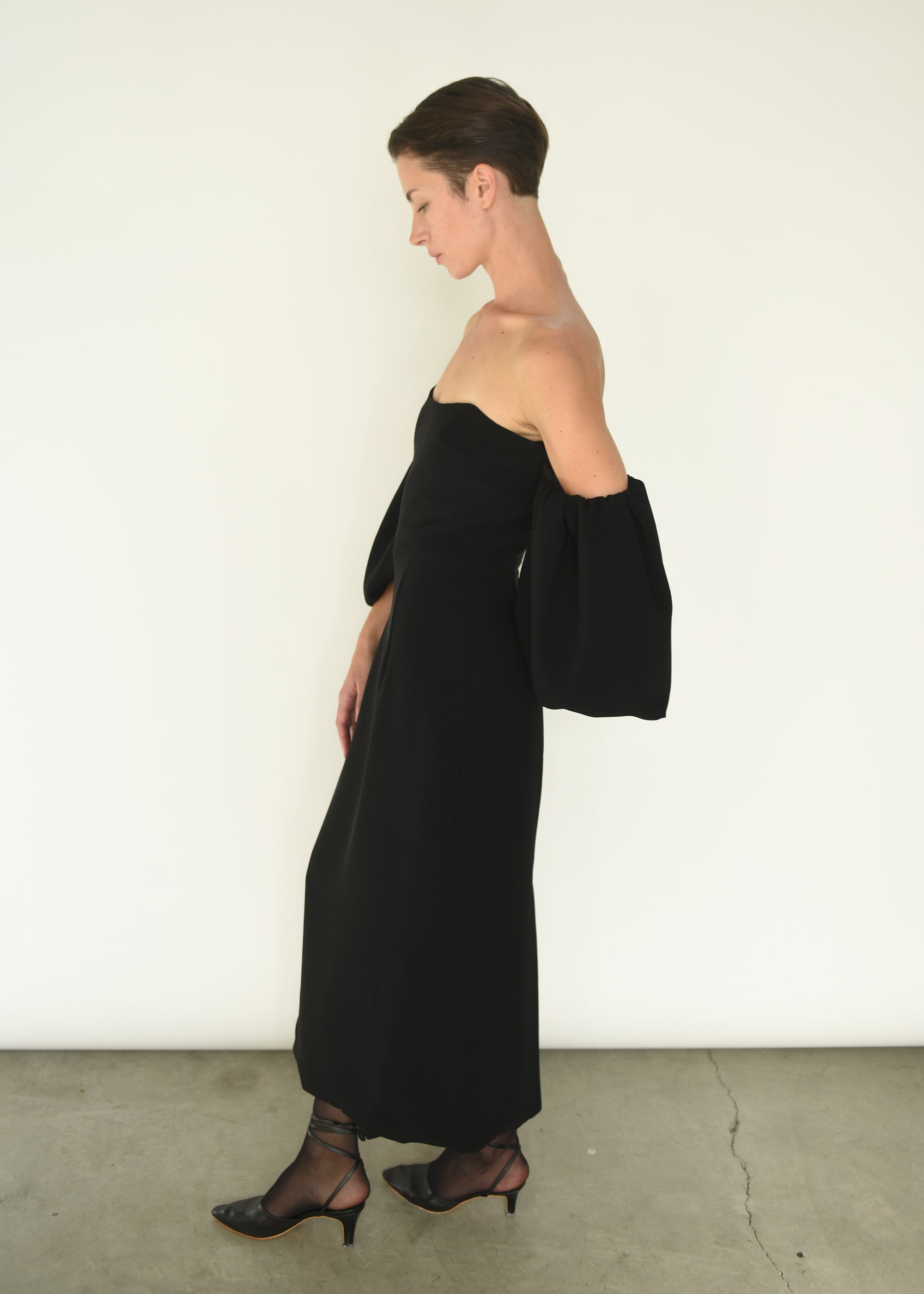 Angled view of the black crepe Kamperett Verona Midi Dress, showing the off-shoulder neckline and full draped sleeves.