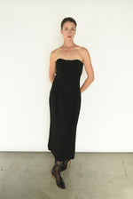 Front view of a model wearing the black crepe Kamperett Verona Midi Dress, an off-shoulder column silhouette with draped sleeves.