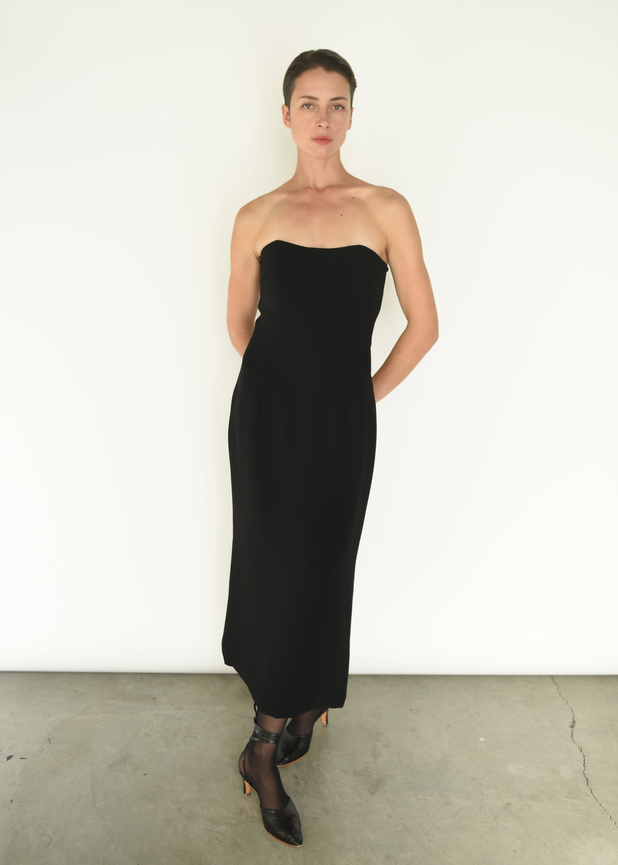 Front view of a model wearing the black crepe Kamperett Verona Midi Dress, an off-shoulder column silhouette with draped sleeves.