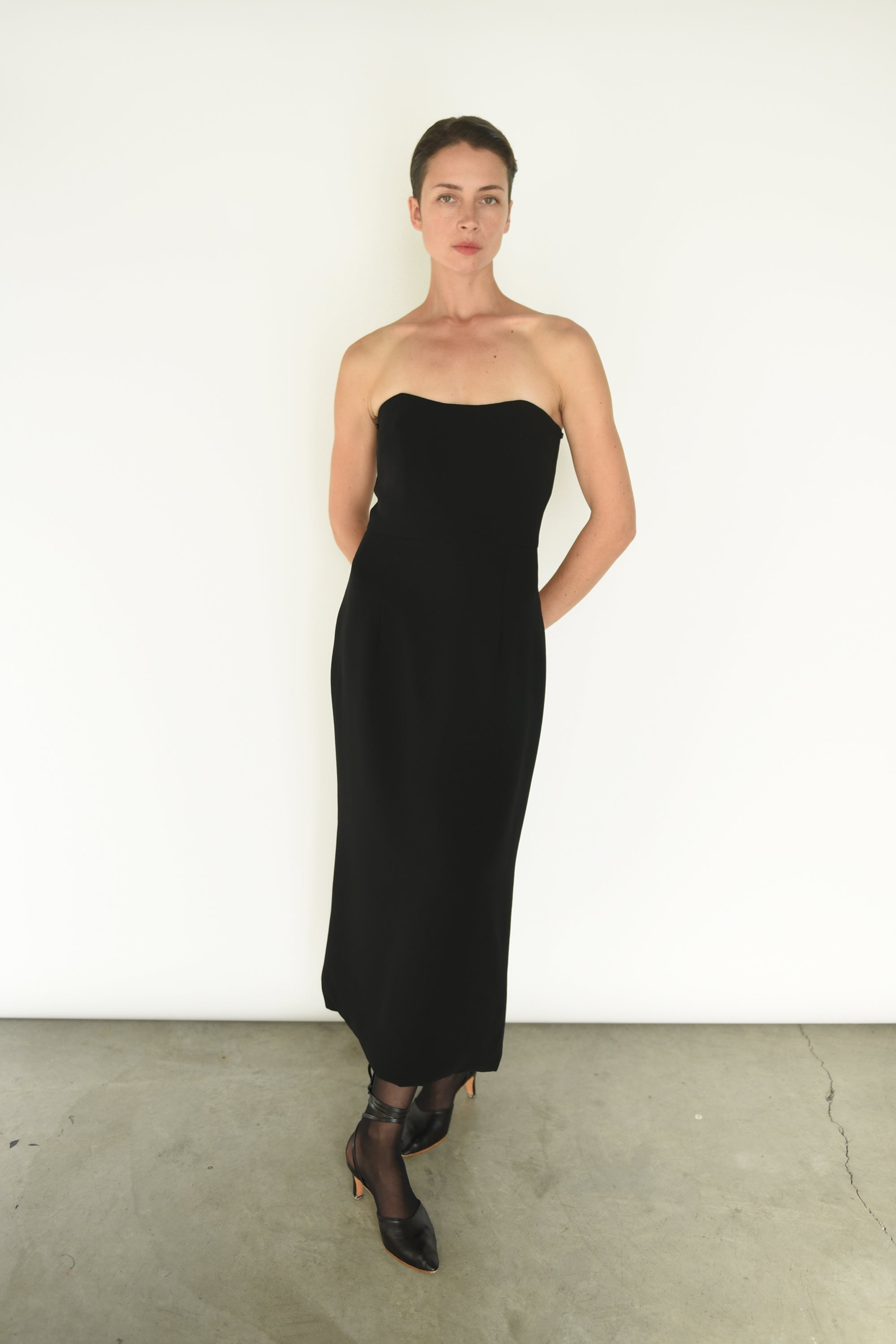 Front view of a model wearing the black crepe Kamperett Verona Midi Dress, an off-shoulder column silhouette with draped sleeves.