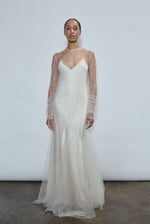 Ivory tulle sheath dress with jewel neckline and sheer long sleeves, falling into a multi-godet hemline. Effortless sculptural silhouette, made in California.