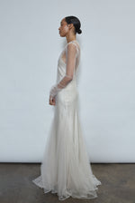 Left profile of ivory sheer tulle sheath dress. Clean column silhouette opens into a sweeping godet skirt. Minimalist aesthetic, ethically made in California.