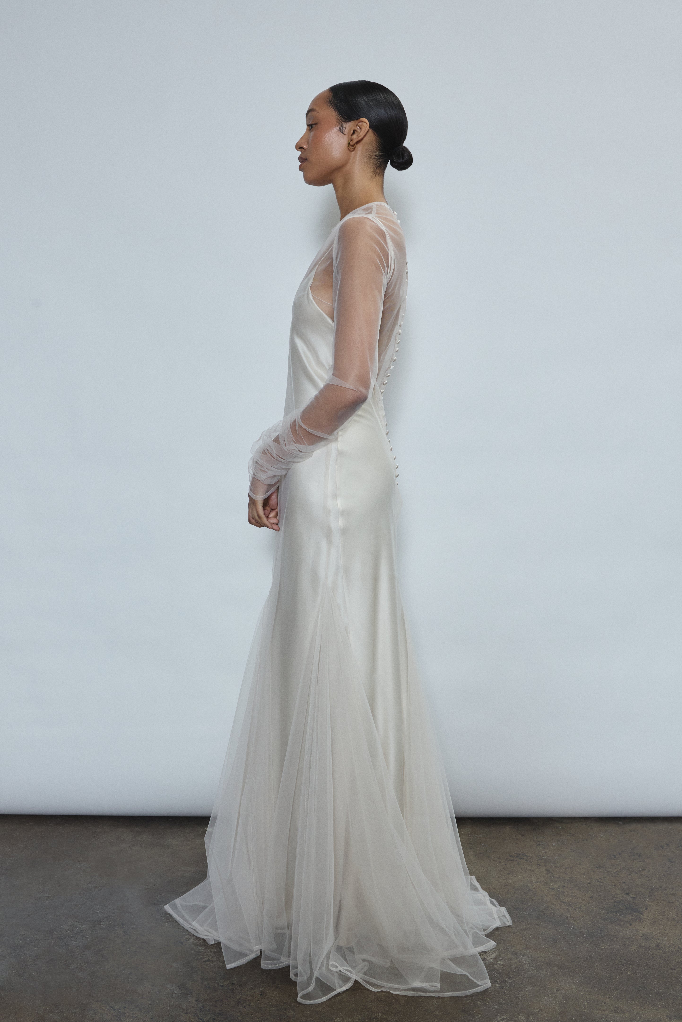 Left profile of ivory sheer tulle sheath dress. Clean column silhouette opens into a sweeping godet skirt. Minimalist aesthetic, ethically made in California.