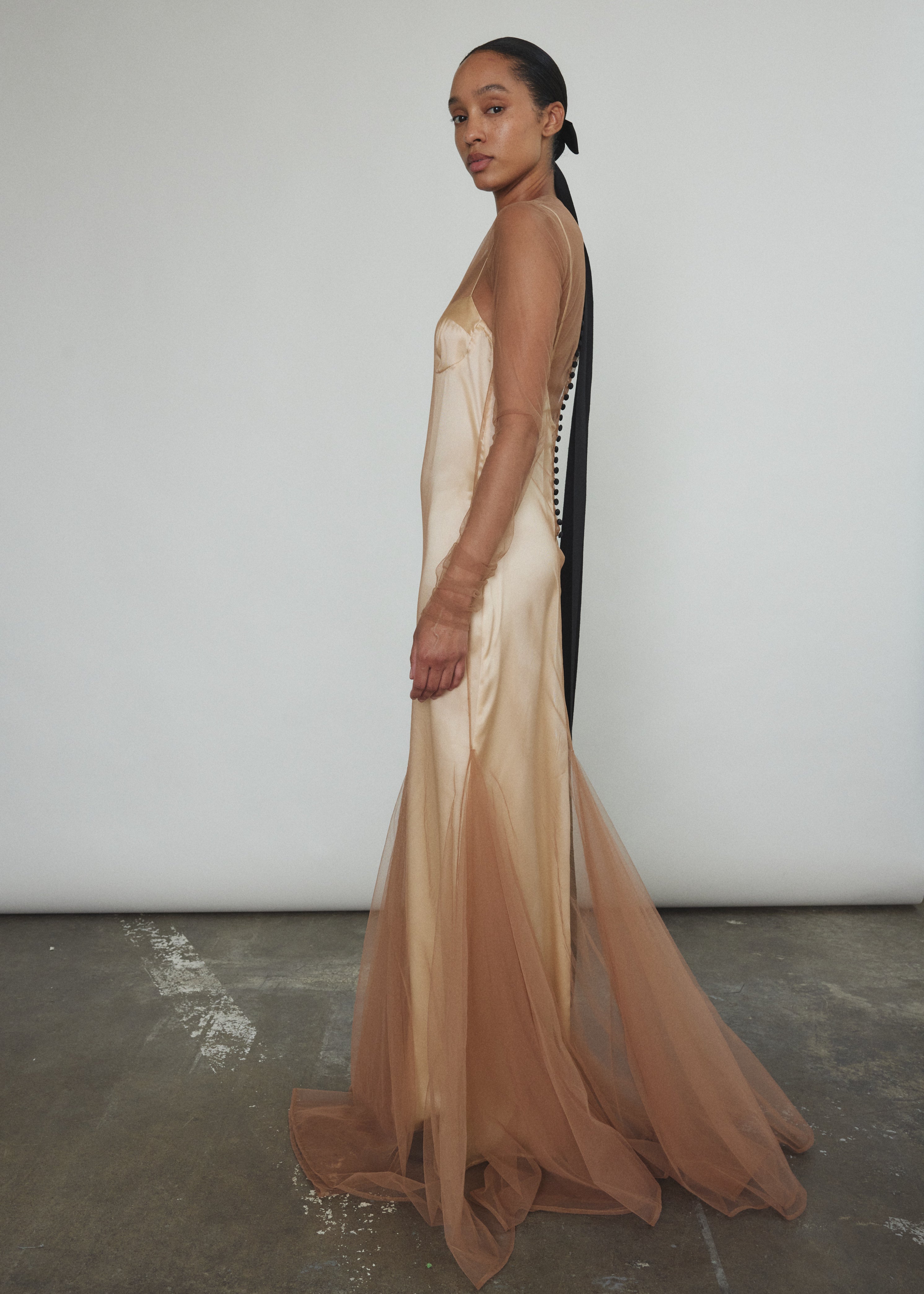 Left profile of Kamperett Violette Tulle Sheath in mocha — sleek sheath silhouette transitions into a sweeping sculptural hem, sheer tulle layer throughout.