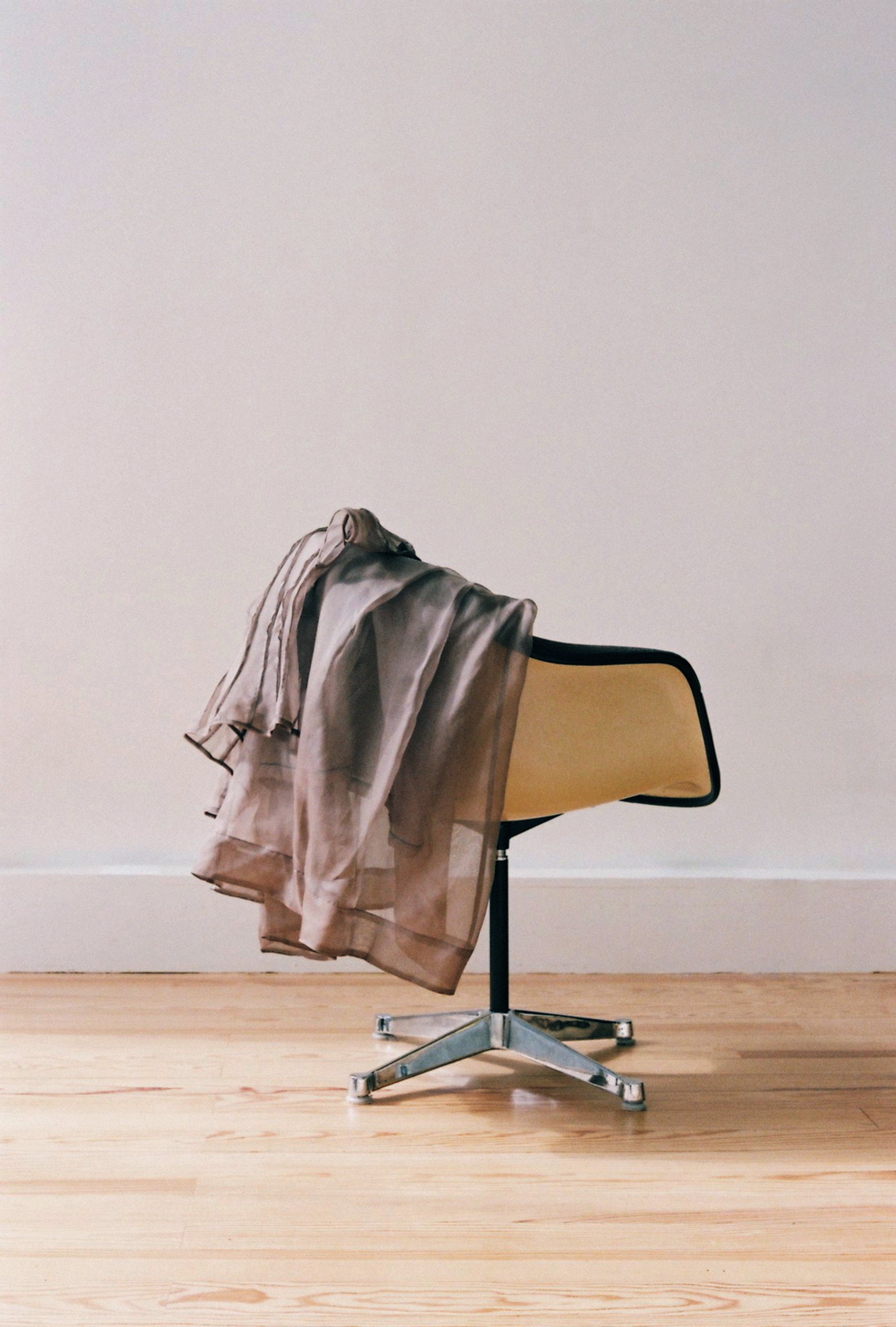 Chair with a brown jacket draped over it against a plain wall.