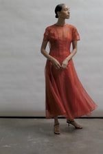 Model wearing the voluminous Kamperett Anemoia Midi dress in Rust silk organza, highlighting the architectural French seams and graceful midi-length silhouette.