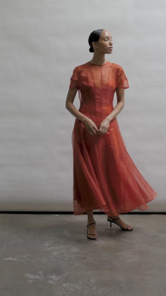 Model wearing the voluminous Kamperett Anemoia Midi dress in Rust silk organza, highlighting the architectural French seams and graceful midi-length silhouette.
