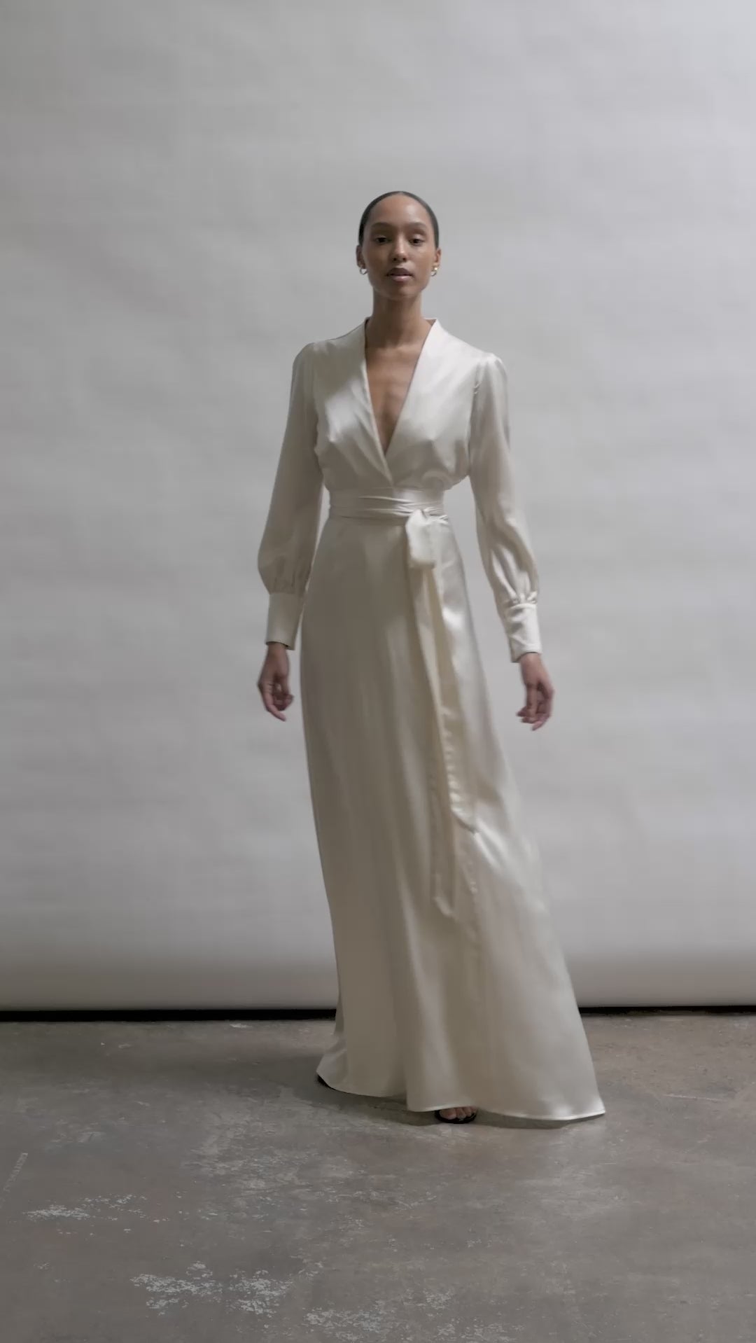 Full-length view of a bride wearing the ivory silk charmeuse Adelaide wrap gown, featuring voluminous sleeves with button cuffs and a plunging neckline.