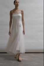 Model wearing the ivory Kamperett Camille Dress, a sheer tulle tea-length overlay featuring adjustable silk corded straps and a voluminous godet-pleated skirt.