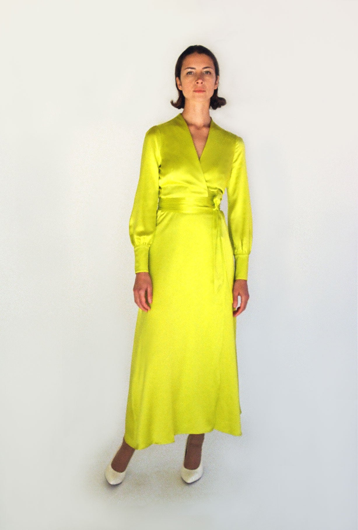 Angled view of the chartreuse satin silk charmeuse Kamperett Adelaide Midi Dress showing the fluid wrap drape.