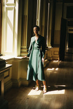 Front view of a model wearing the dark green matte silk charmeuse Kamperett Adelaide Midi Dress, a wrap dress with plunging neckline and full sleeves.
