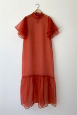 Front view of a model wearing the rust silk organza Kamperett Barre Dress, with exaggerated ruffle hem and tiered sleeves.