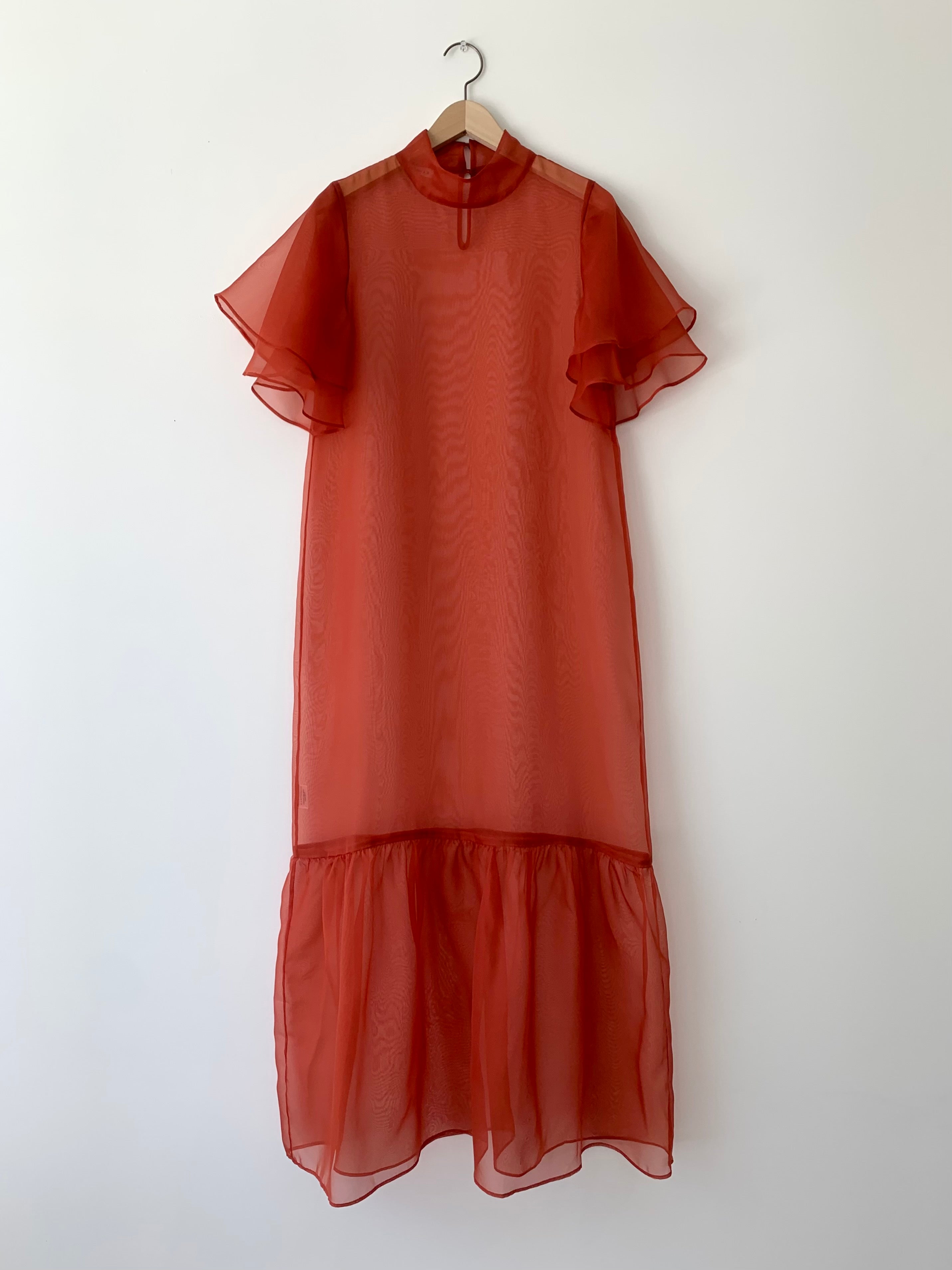 Front view of a model wearing the rust silk organza Kamperett Barre Dress, with exaggerated ruffle hem and tiered sleeves.