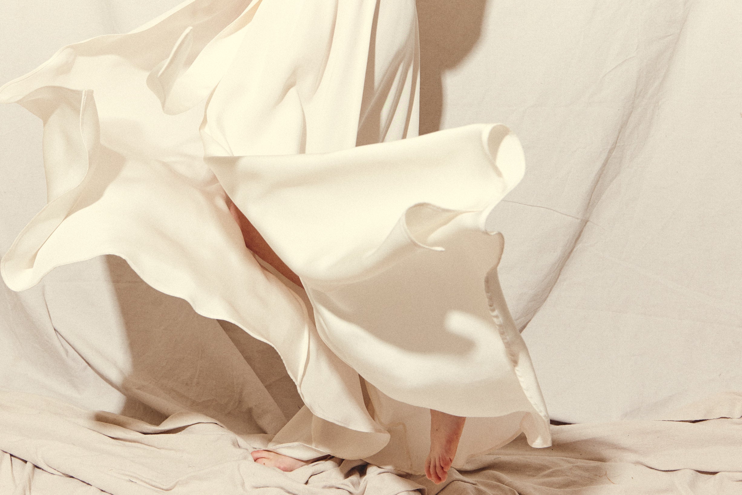 Motion shot of the alabaster four-ply silk crepe Kamperett Loretta Gown, capturing the fluid wrap drape.