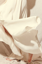 Motion shot of the alabaster four-ply silk crepe Kamperett Loretta Gown, capturing the fluid wrap drape.