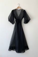 Front view of a model wearing the black silk organza Kamperett Loretta Midi Dress, a wrap with elbow-length sleeves and shoulder ruffle.