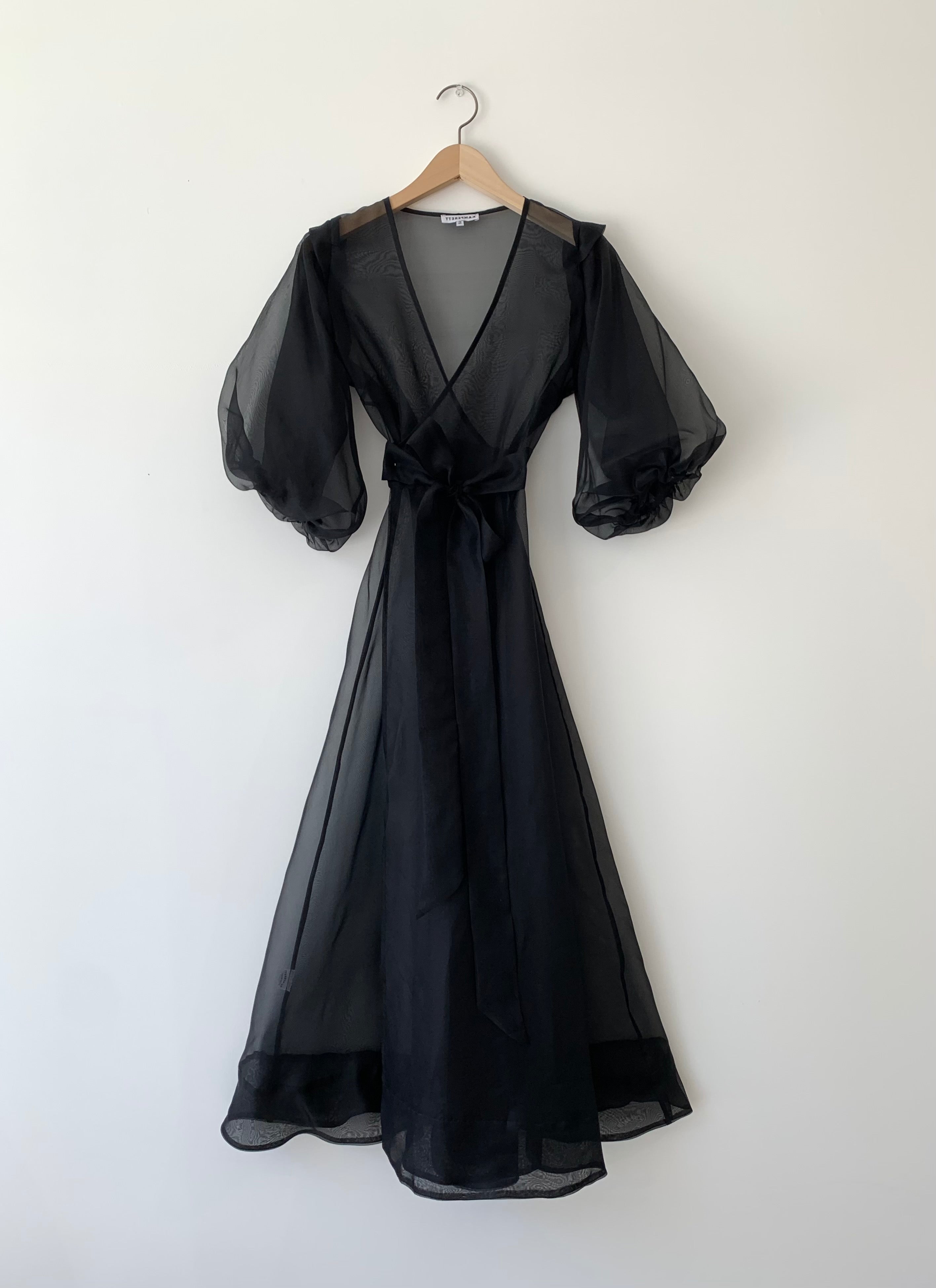 Front view of a model wearing the black silk organza Kamperett Loretta Midi Dress, a wrap with elbow-length sleeves and shoulder ruffle.