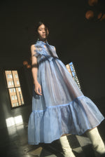 Front view of a model wearing the cornflower silk organza Kamperett Mae Dress, a midi with empire waist and qipao-inspired tie front.