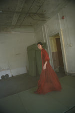 Angled view of the rust silk organza Kamperett Meiere Gown with fitted waist and mock neck.