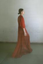 Front view of a model wearing the rust silk organza Kamperett Meiere Gown, with architectural sleeves and fitted waist.