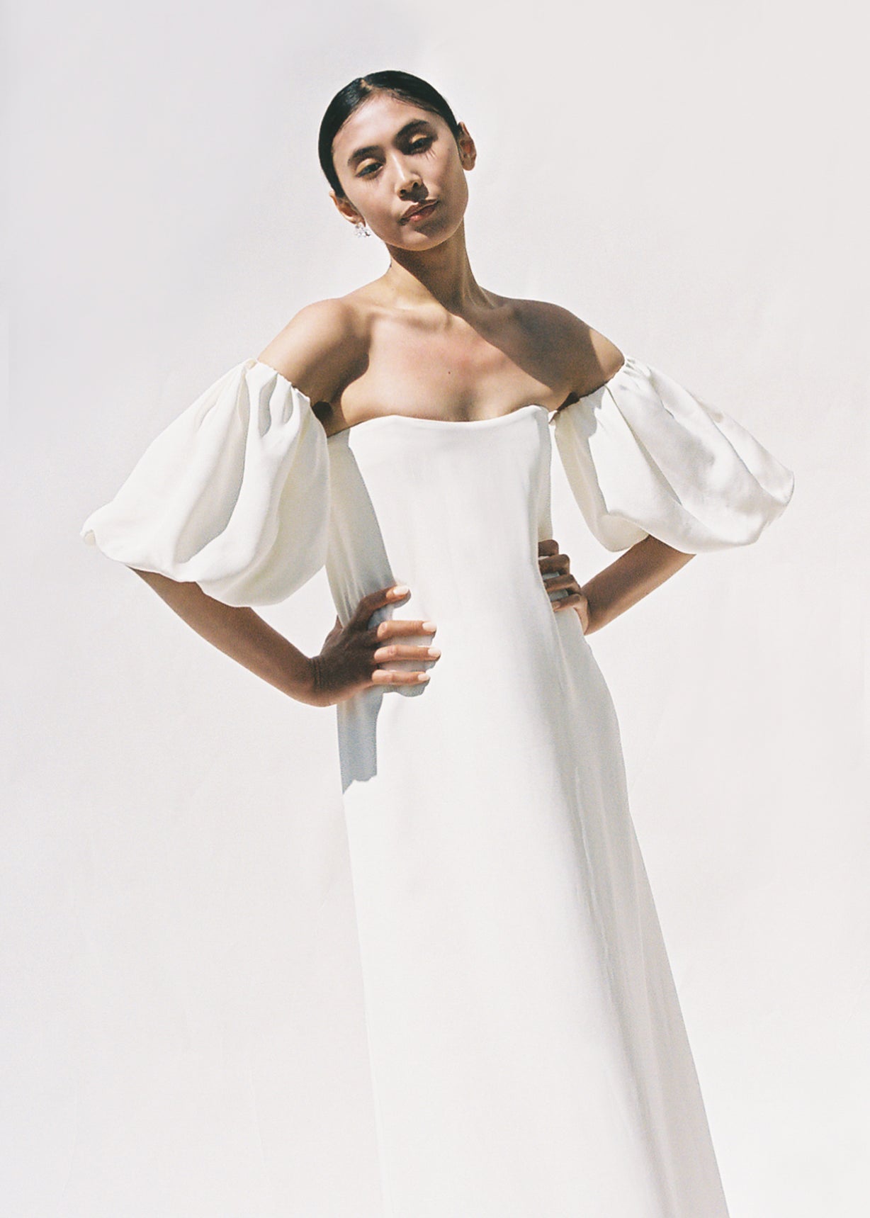 Editorial film image of a bride wearing the alabaster silk crepe Kamperett Verona Gown, an off-shoulder maxi with detachable draped sleeves.