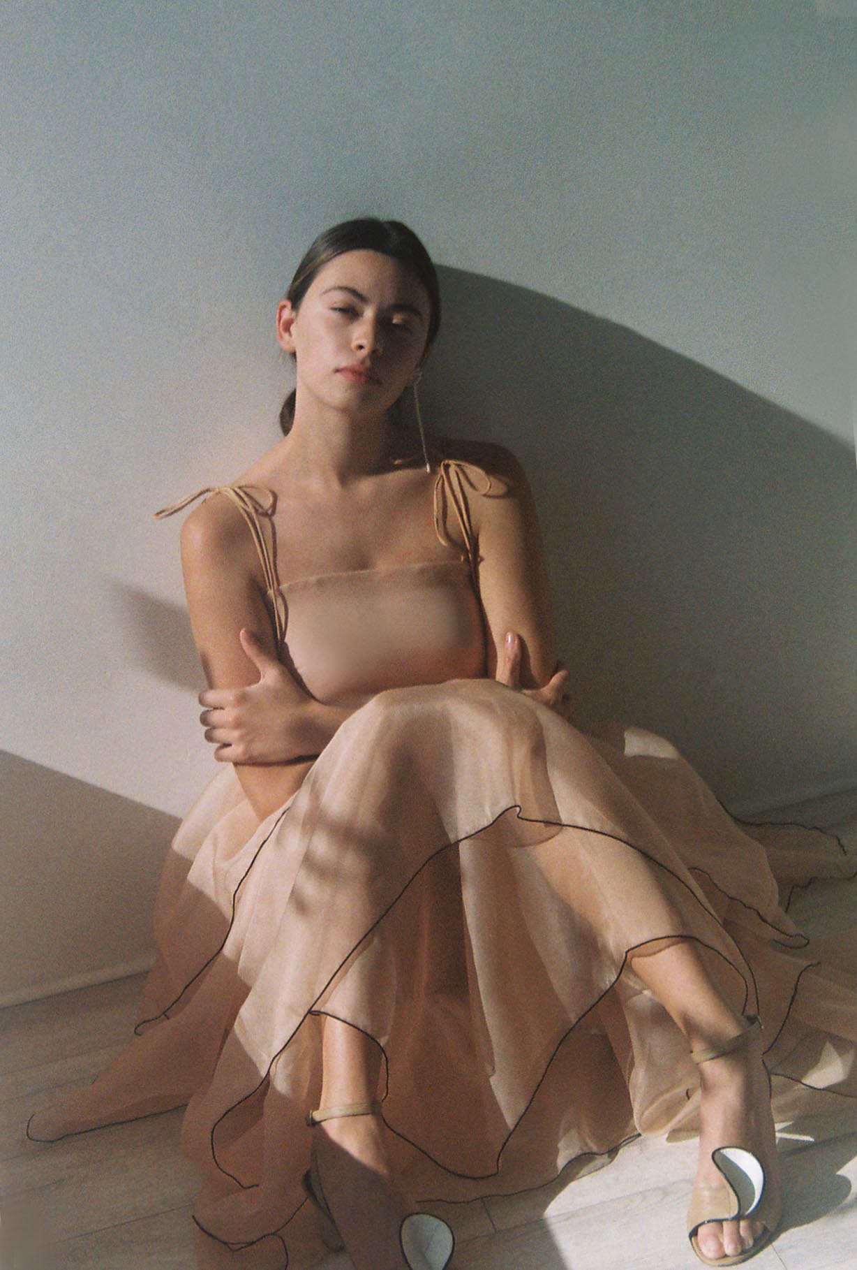 Front view of a model wearing the blush silk organza Kamperett Laurence Midi Dress, a tiered midi with corded shoulder ties and black pearl edge trim.